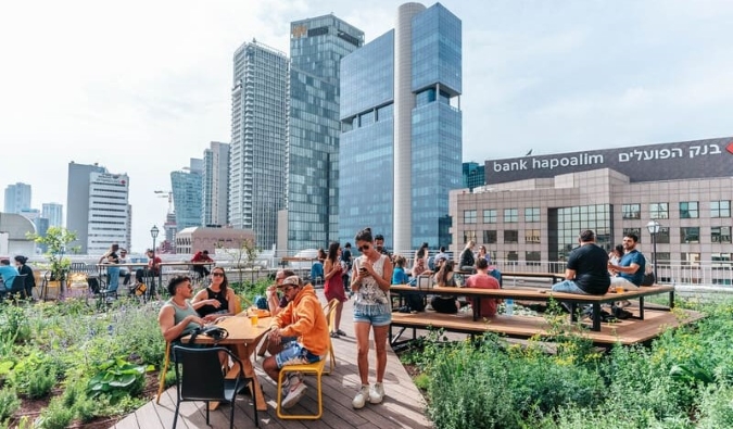 People hanging out on the rooftop hostel of Abraham Tel Aviv hostel, with skyscrapers in the background, in Tel Aviv, Israel