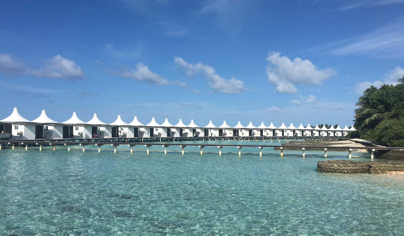 Row of white huts in a row on a boardwalk over the water at a resort in the Maldives