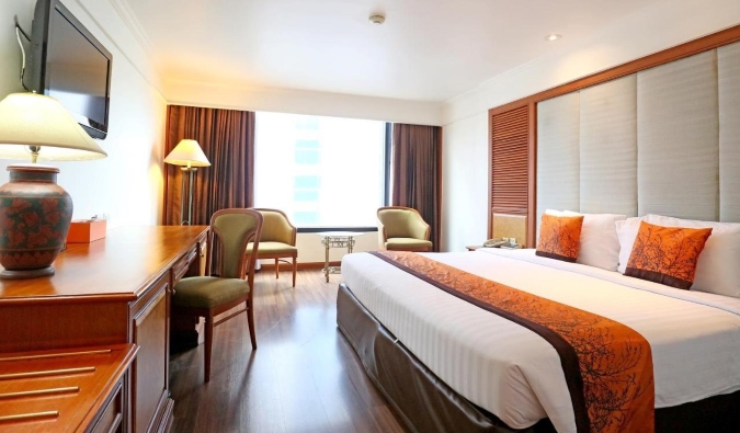 A queen bed in a warmly designed room with a desk and seating area at Bangkok Lotus hotel in Bangkok, Thailand