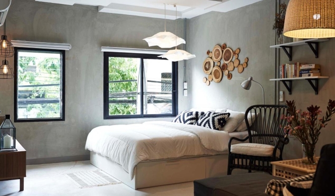 A double bed in a hotel room with large windows, brushed concrete windows, and wooden accenting on the walls at House of Phraya Jasaen hotel in Bangkok, Thailand
