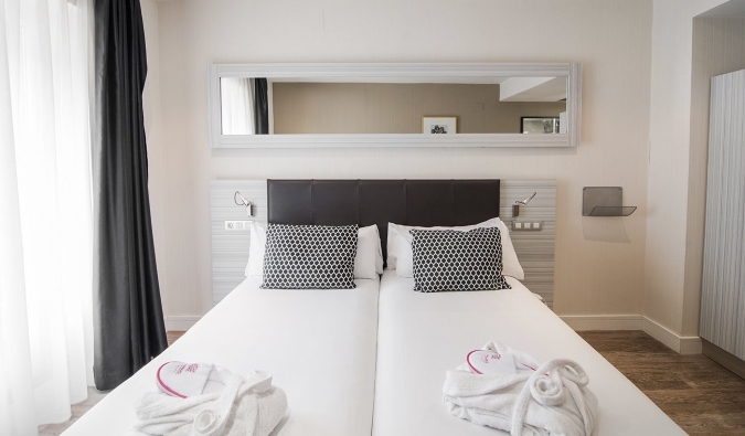 A mirror hangs above a double bed with white sheets and bath towels arranged in a decorative manner at Petit Palace Puerta del Sol hotel in Madrid, Spain