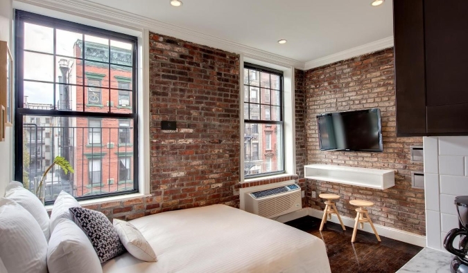 Sunny hotel room with exposed brick walls, a double bed, and a flatscreen TV on the walls at East Village Hotel in NYC